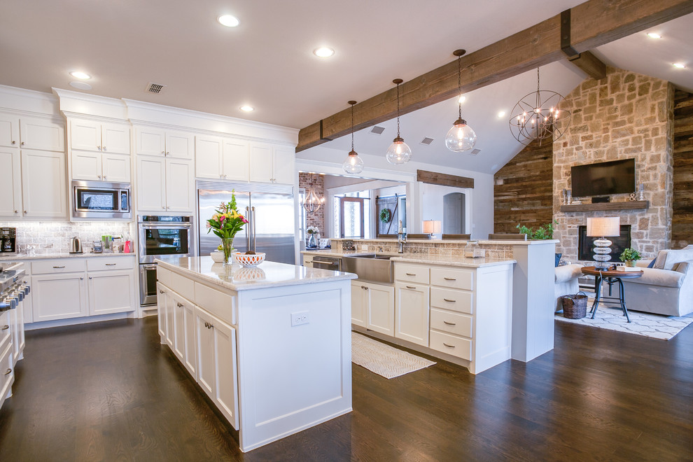 This is an example of a large country u-shaped open plan kitchen in Dallas with shaker cabinets, white cabinets, marble benchtops, grey splashback, stone tile splashback, stainless steel appliances, dark hardwood floors, multiple islands, a farmhouse sink and brown floor.