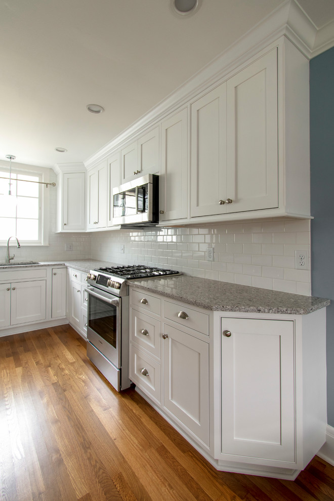 Mid-sized transitional l-shaped eat-in kitchen in Milwaukee with an undermount sink, beaded inset cabinets, white cabinets, quartz benchtops, white splashback, subway tile splashback, stainless steel appliances, medium hardwood floors, with island, brown floor and beige benchtop.