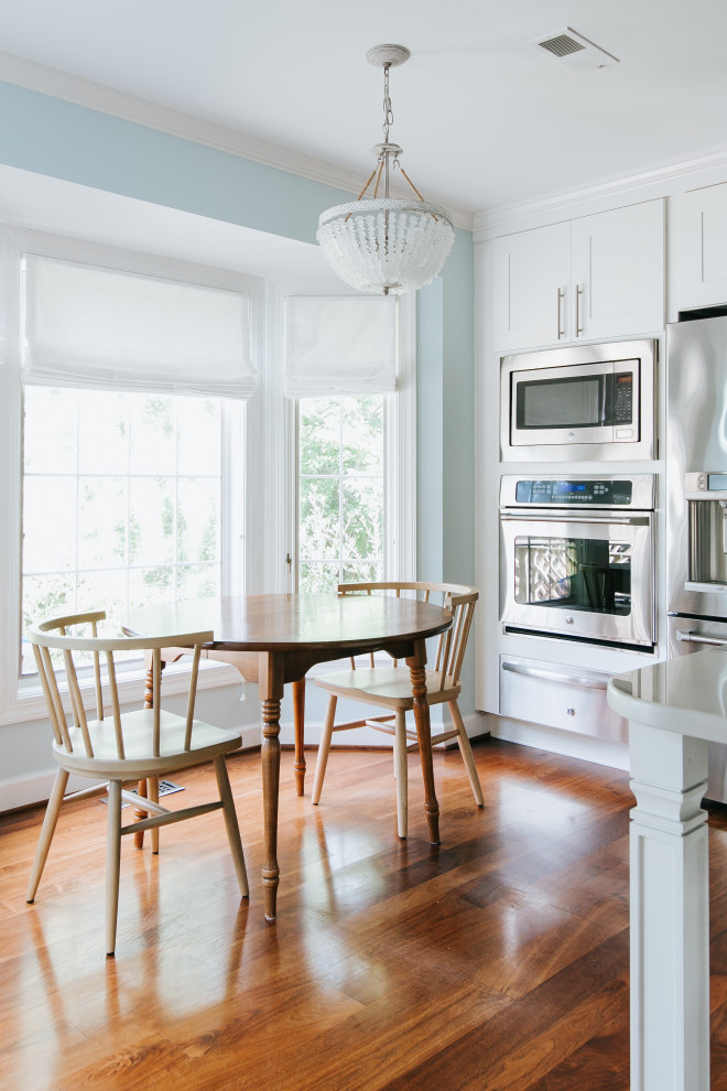 Immagine di una grande cucina costiera con ante bianche, paraspruzzi blu, elettrodomestici in acciaio inossidabile e pavimento marrone