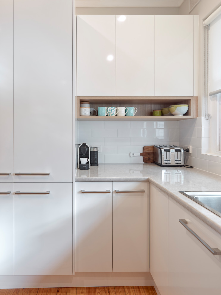 This is an example of a mid-sized contemporary u-shaped eat-in kitchen in Other with a double-bowl sink, white cabinets, laminate benchtops, white splashback, subway tile splashback, stainless steel appliances, medium hardwood floors, no island, orange floor and beige benchtop.