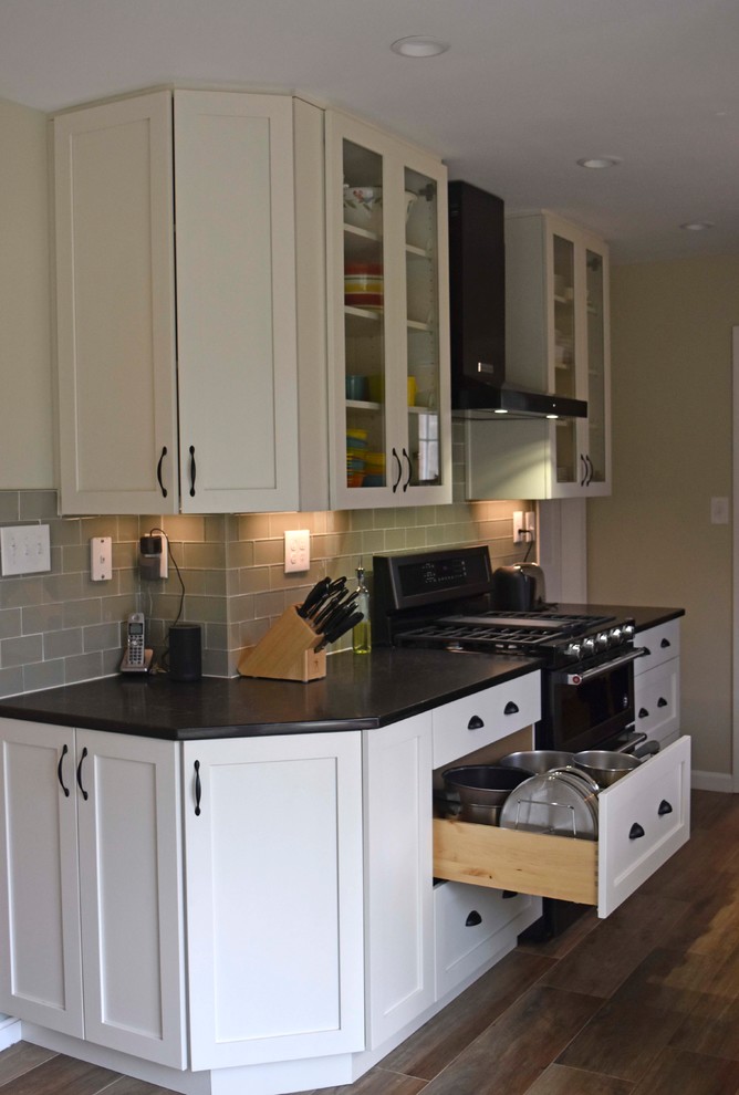 Example of a mid-sized transitional galley laminate floor and brown floor enclosed kitchen design in DC Metro with a farmhouse sink, shaker cabinets, white cabinets, granite countertops, gray backsplash, subway tile backsplash, stainless steel appliances, no island and black countertops