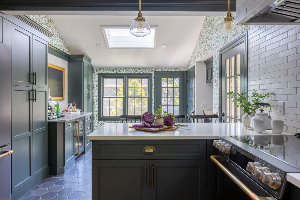 Example of a transitional u-shaped medium tone wood floor and brown floor kitchen design in Boston with a farmhouse sink, shaker cabinets, green cabinets, quartz countertops, white backsplash, ceramic backsplash, black appliances, a peninsula and white countertops