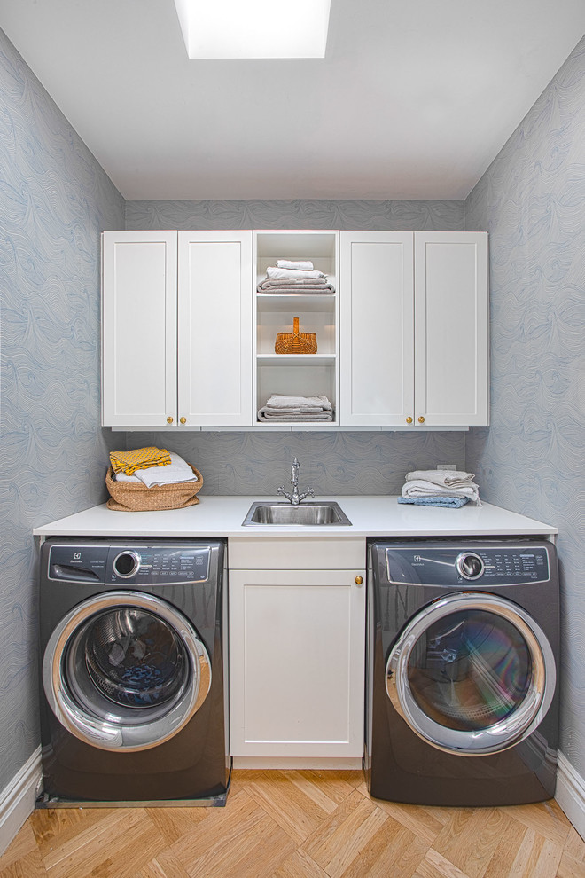 Inspiration for a small transitional single-wall dedicated laundry room in New York with a drop-in sink, shaker cabinets, white cabinets, quartz benchtops, blue walls, medium hardwood floors, a side-by-side washer and dryer, brown floor and white benchtop.