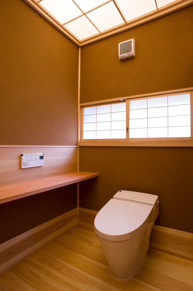 Design ideas for an asian powder room in Other with a one-piece toilet, brown walls, light hardwood floors and orange floor.
