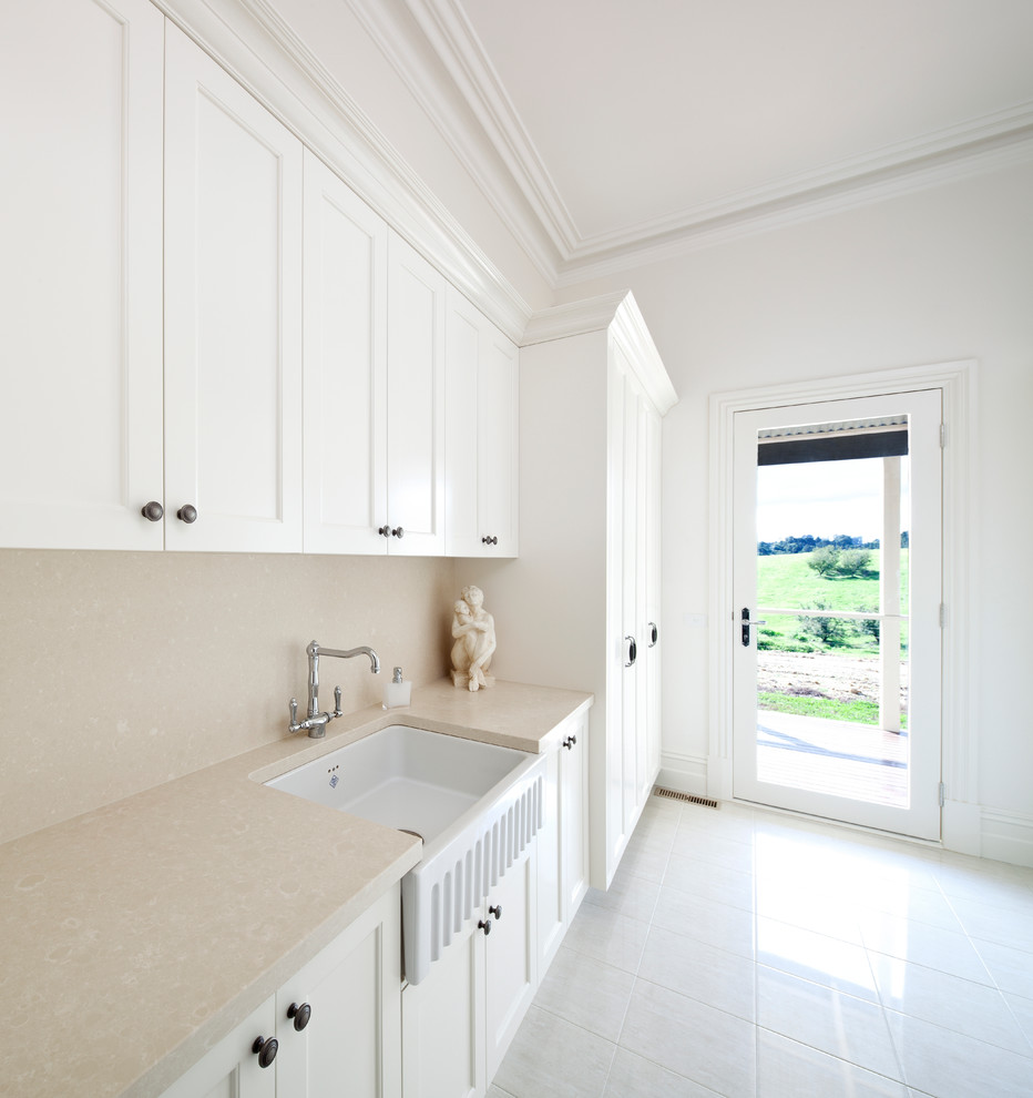 Photo of a large transitional galley dedicated laundry room in Melbourne with a farmhouse sink, shaker cabinets, white cabinets and white walls.