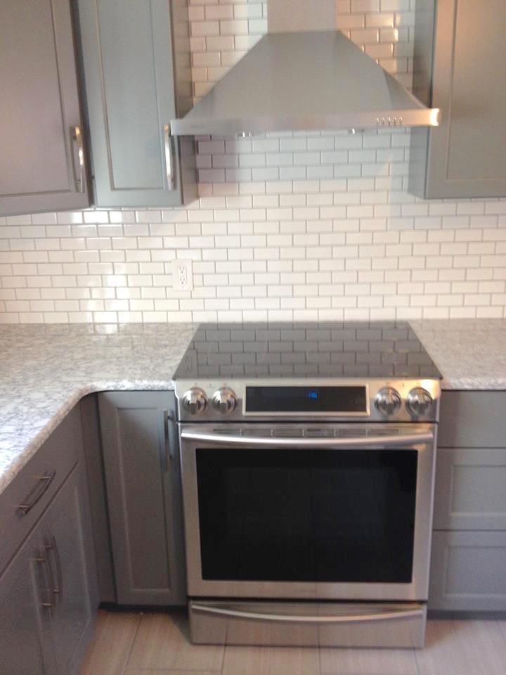 Mid-sized transitional l-shaped ceramic tile eat-in kitchen photo in Boston with a farmhouse sink, recessed-panel cabinets, gray cabinets, granite countertops, white backsplash, subway tile backsplash, stainless steel appliances and an island
