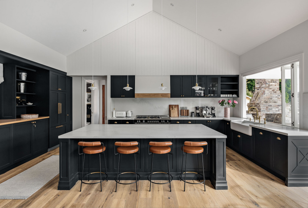 Design ideas for a transitional u-shaped kitchen in Wollongong with a farmhouse sink, shaker cabinets, black cabinets, grey splashback, stone slab splashback, panelled appliances, light hardwood floors, with island, beige floor, grey benchtop and vaulted.