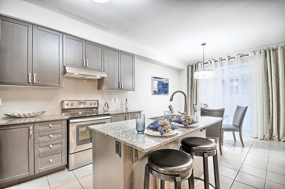 Mid-sized transitional l-shaped ceramic tile and beige floor open concept kitchen photo in Toronto with an undermount sink, shaker cabinets, gray cabinets, granite countertops, beige backsplash, mosaic tile backsplash, stainless steel appliances and an island