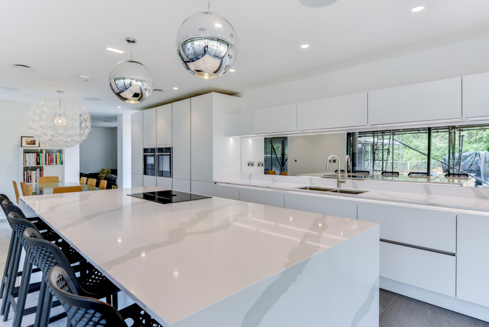 Exempel på ett stort modernt vit linjärt vitt kök och matrum, med en dubbel diskho, släta luckor, vita skåp, bänkskiva i kvartsit, flerfärgad stänkskydd, spegel som stänkskydd, svarta vitvaror, klinkergolv i porslin, en köksö och grått golv