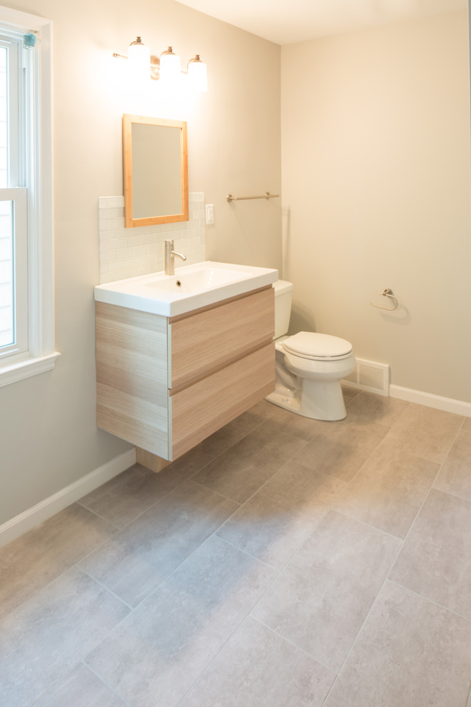 Inspiration for a mid-sized arts and crafts bathroom in Detroit with flat-panel cabinets, light wood cabinets, a one-piece toilet, white tile, subway tile, beige walls, porcelain floors, an integrated sink, grey floor and solid surface benchtops.