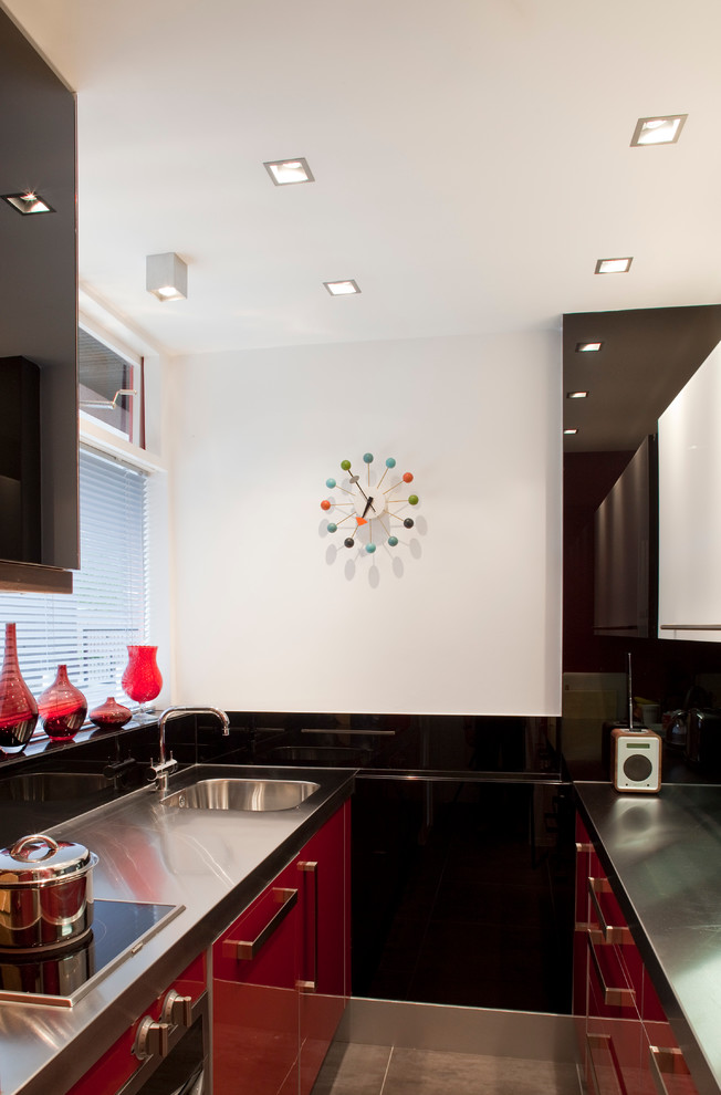 Inspiration for a small modern galley enclosed kitchen in London with an integrated sink, flat-panel cabinets, red cabinets, stainless steel worktops, black splashback, glass sheet splashback, stainless steel appliances, porcelain flooring and multiple islands.
