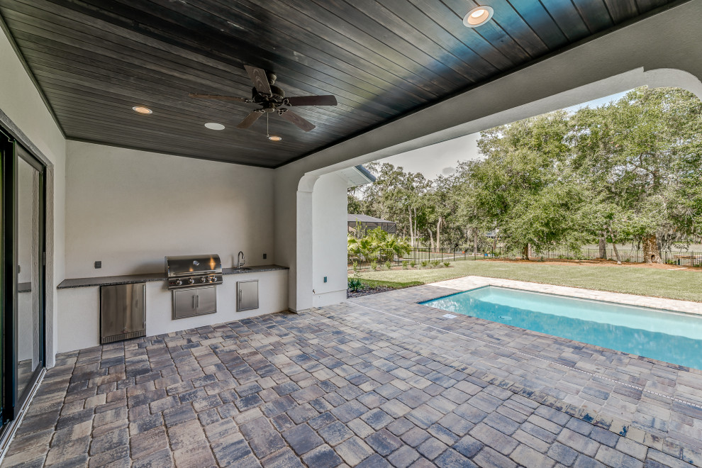 Cette image montre un grand porche d'entrée de maison arrière méditerranéen avec une cuisine d'été, des pavés en béton et une extension de toiture.