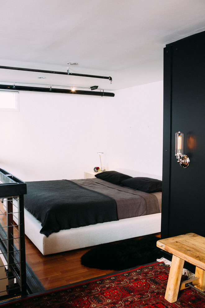 Mid-sized industrial loft-style bedroom in Los Angeles with medium hardwood floors, white walls and no fireplace.