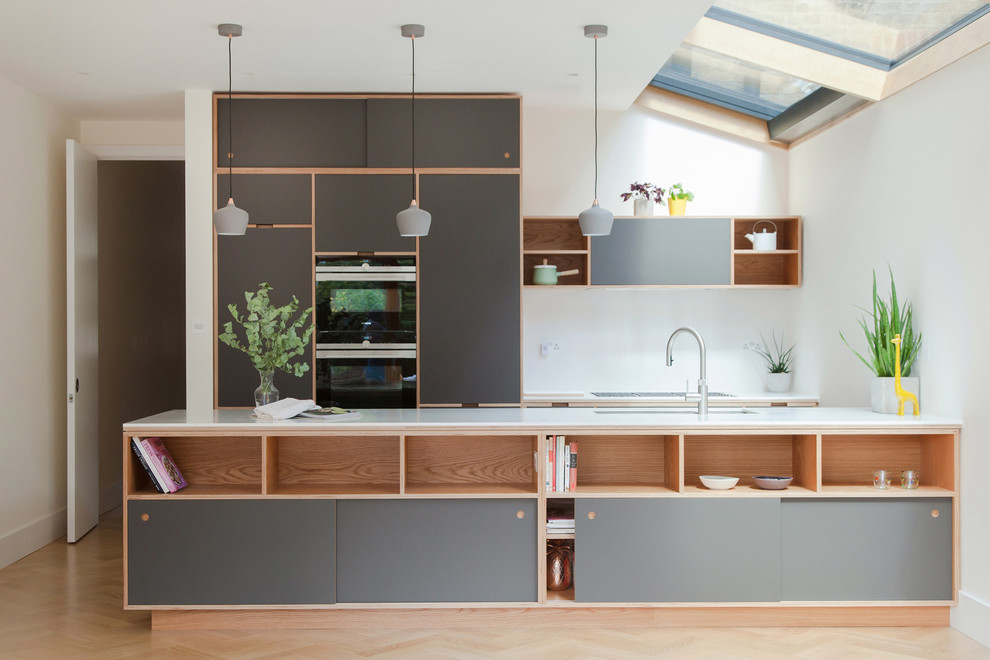 Photo of a mid-sized scandinavian single-wall kitchen in London with flat-panel cabinets, grey cabinets, beige floor, white benchtop, an undermount sink, white splashback, black appliances, light hardwood floors and a peninsula.
