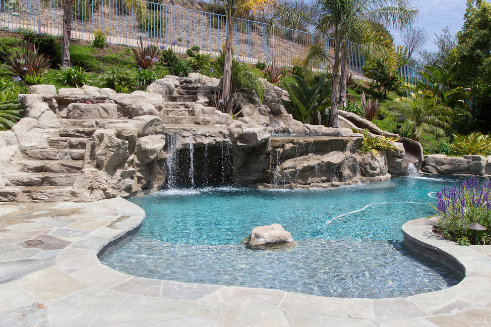 Large tropical backyard custom-shaped natural pool in Los Angeles with a water slide and natural stone pavers.