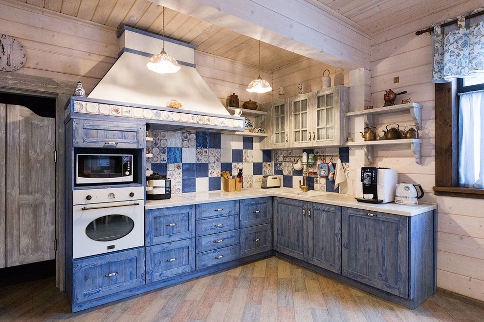 Photo of a large country l-shaped open plan kitchen in Moscow with raised-panel cabinets, blue cabinets, wood benchtops, ceramic splashback, white appliances, porcelain floors, with island, a drop-in sink and multi-coloured splashback.