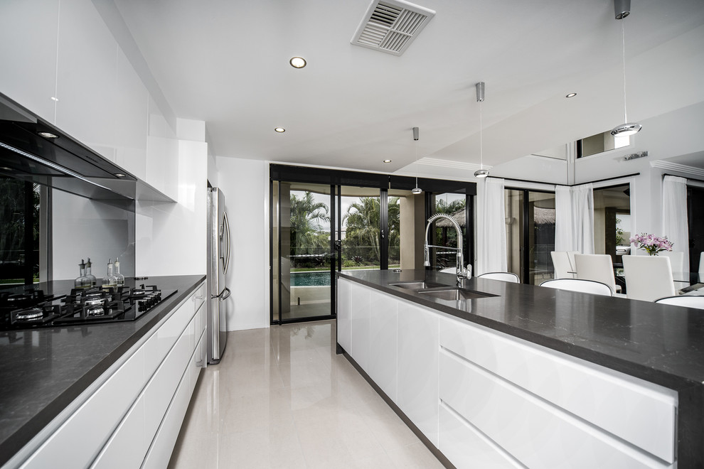 Design ideas for a mid-sized modern l-shaped open plan kitchen in Gold Coast - Tweed with an undermount sink, flat-panel cabinets, white cabinets, quartz benchtops, mirror splashback, stainless steel appliances, porcelain floors, with island and white floor.