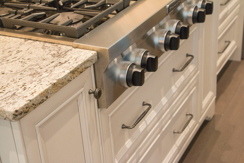 Large transitional l-shaped home design photo with a double-bowl sink, shaker cabinets, white cabinets, beige backsplash, stainless steel appliances and an island
