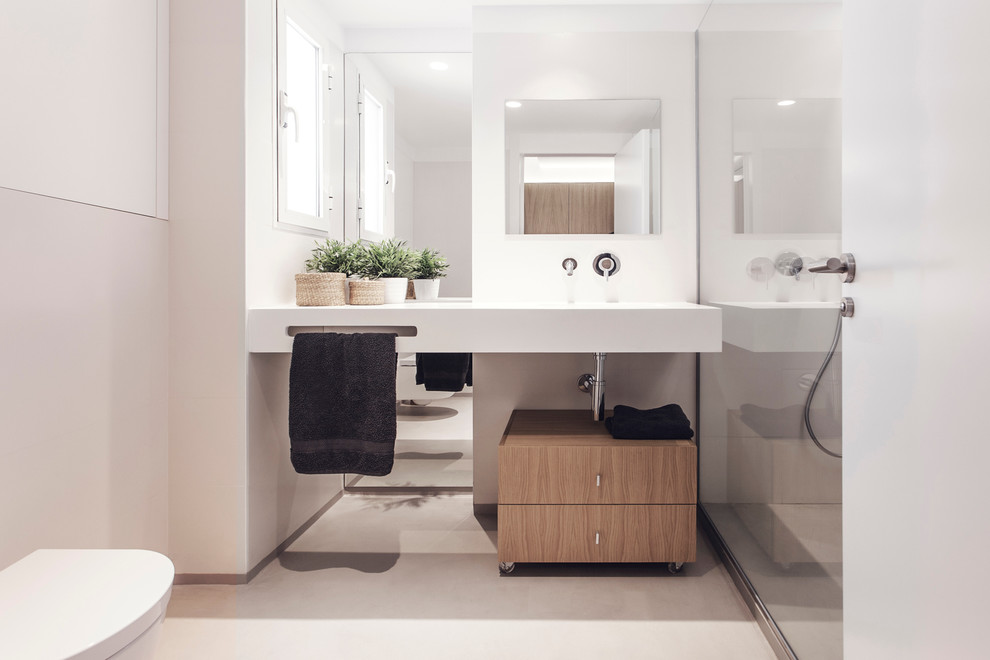 Design ideas for a mid-sized contemporary powder room in Valencia with a trough sink, flat-panel cabinets, light wood cabinets, a one-piece toilet and white walls.