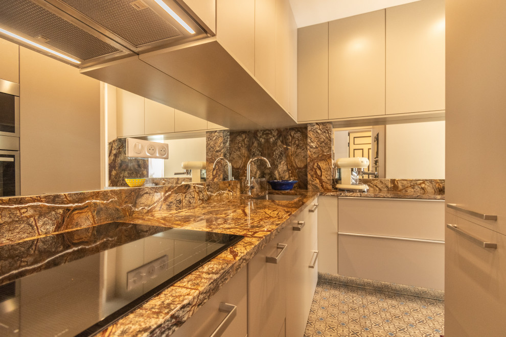 This is an example of a small transitional l-shaped open plan kitchen in Nice with an undermount sink, flat-panel cabinets, beige cabinets, granite benchtops, panelled appliances, cement tiles, blue floor and brown benchtop.