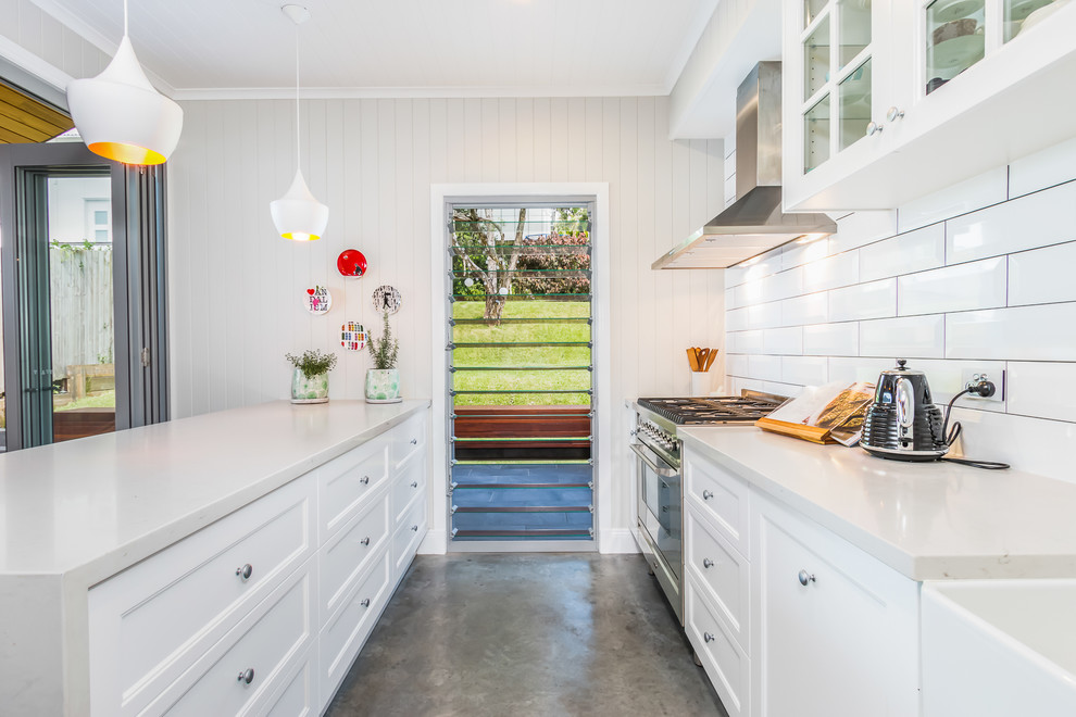 This is an example of a mid-sized transitional galley eat-in kitchen in Brisbane with a farmhouse sink, shaker cabinets, white cabinets, quartz benchtops, white splashback, subway tile splashback, stainless steel appliances, concrete floors, with island and white benchtop.