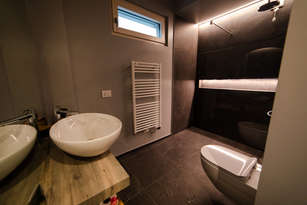 Exempel på ett litet nordiskt brun brunt badrum med dusch, med släta luckor, grå skåp, en toalettstol med hel cisternkåpa, svart kakel, porslinskakel, grå väggar, klinkergolv i porslin, ett fristående handfat, träbänkskiva, svart golv, ett fristående badkar, en kantlös dusch och med dusch som är öppen
