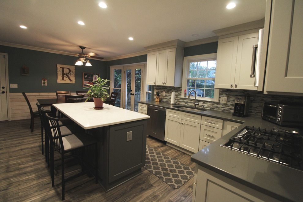 Mid-sized transitional u-shaped medium tone wood floor and brown floor eat-in kitchen photo in Atlanta with a drop-in sink, white cabinets, granite countertops, gray backsplash, matchstick tile backsplash, stainless steel appliances, an island, shaker cabinets and gray countertops