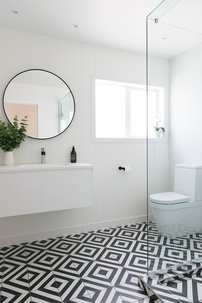 Inspiration for a contemporary 3/4 bathroom in Auckland with flat-panel cabinets, white cabinets, a corner shower, a two-piece toilet, white tile, white walls, a wall-mount sink, black floor, a hinged shower door and white benchtops.