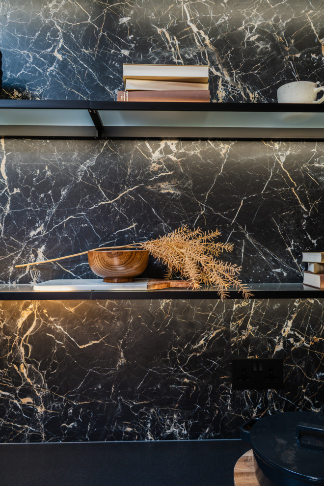 Photo of a medium sized modern l-shaped open plan kitchen in London with a built-in sink, glass-front cabinets, black cabinets, marble worktops, black splashback, stone slab splashback, black appliances, porcelain flooring, an island, grey floors and black worktops.