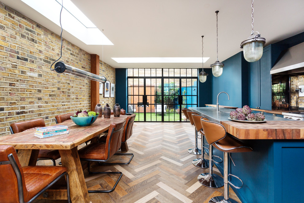 Design ideas for a mid-sized eclectic l-shaped open plan kitchen in London with a farmhouse sink, shaker cabinets, blue cabinets, zinc benchtops, mirror splashback, stainless steel appliances, dark hardwood floors, with island, multi-coloured floor and grey benchtop.