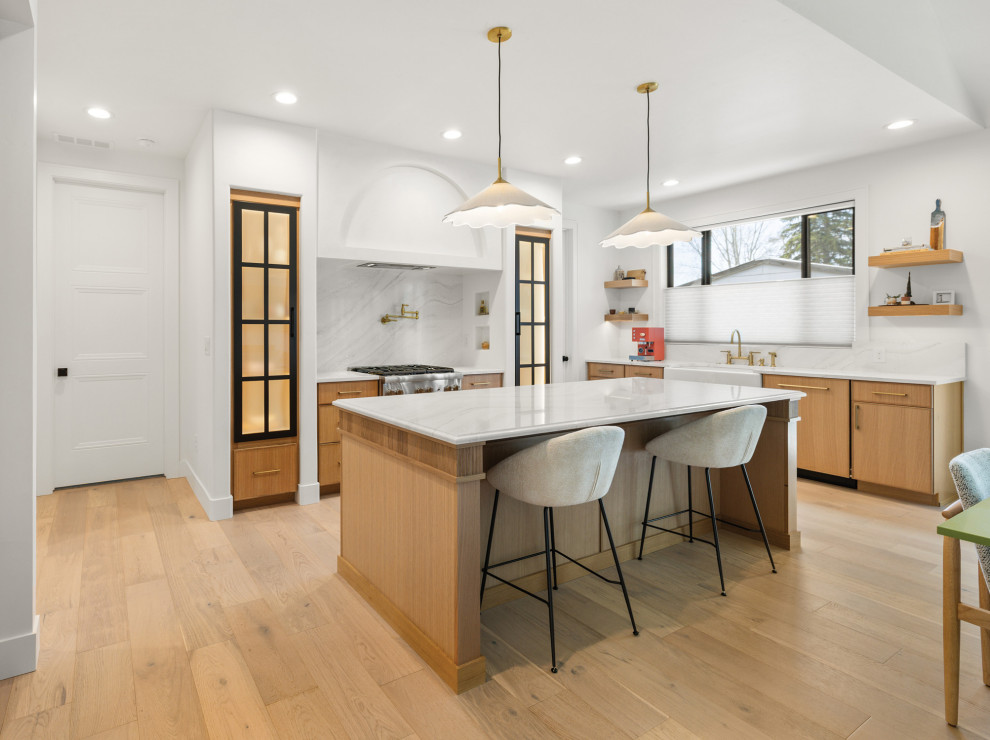 Example of a transitional l-shaped light wood floor and beige floor kitchen design with a farmhouse sink, flat-panel cabinets, medium tone wood cabinets, white backsplash, stone slab backsplash, stainless steel appliances, an island and white countertops