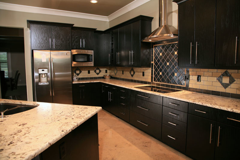 Inspiration for a large transitional l-shaped porcelain tile eat-in kitchen remodel with a double-bowl sink, flat-panel cabinets, black cabinets, granite countertops, beige backsplash, subway tile backsplash, stainless steel appliances and an island