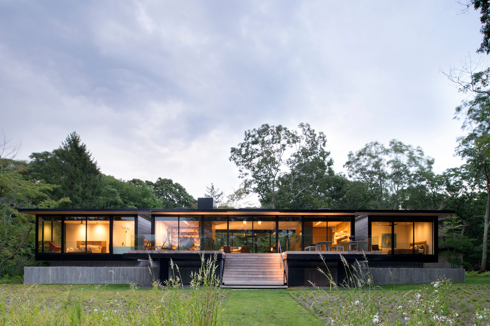 This is an example of a mid-sized modern one-storey glass house exterior in New York with a flat roof.