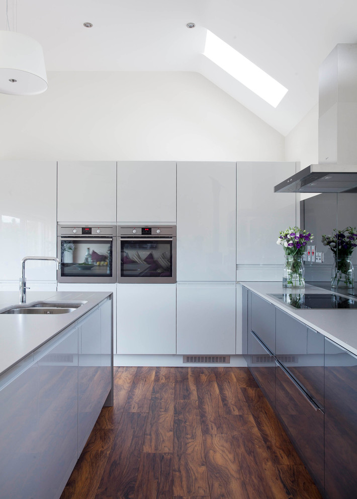 Inspiration for a mid-sized contemporary l-shaped open plan kitchen in Other with an integrated sink, flat-panel cabinets, grey cabinets, quartzite benchtops, grey splashback, mirror splashback, stainless steel appliances, medium hardwood floors and with island.