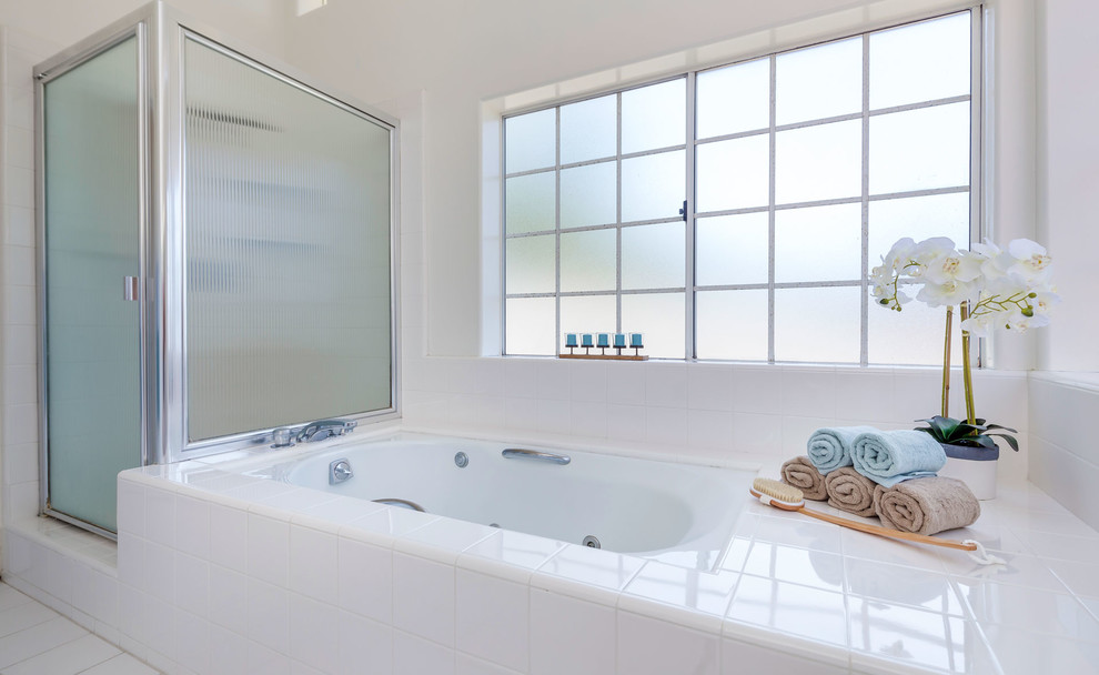 Mid-sized beach style master bathroom in Los Angeles with flat-panel cabinets, white cabinets, a corner shower, white tile, ceramic tile, tile benchtops, a hinged shower door, a hot tub, a one-piece toilet, white walls, ceramic floors, a drop-in sink and white floor.