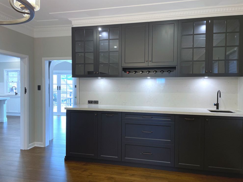 Photo of a mid-sized traditional single-wall wet bar in Sydney with an undermount sink, recessed-panel cabinets, black cabinets, quartz benchtops, white splashback, engineered quartz splashback, medium hardwood floors, brown floor and white benchtop.