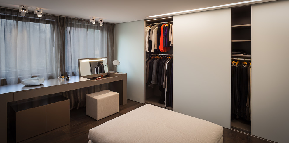 Photo of a mid-sized contemporary gender-neutral dressing room in Cologne with glass-front cabinets, white cabinets and dark hardwood floors.