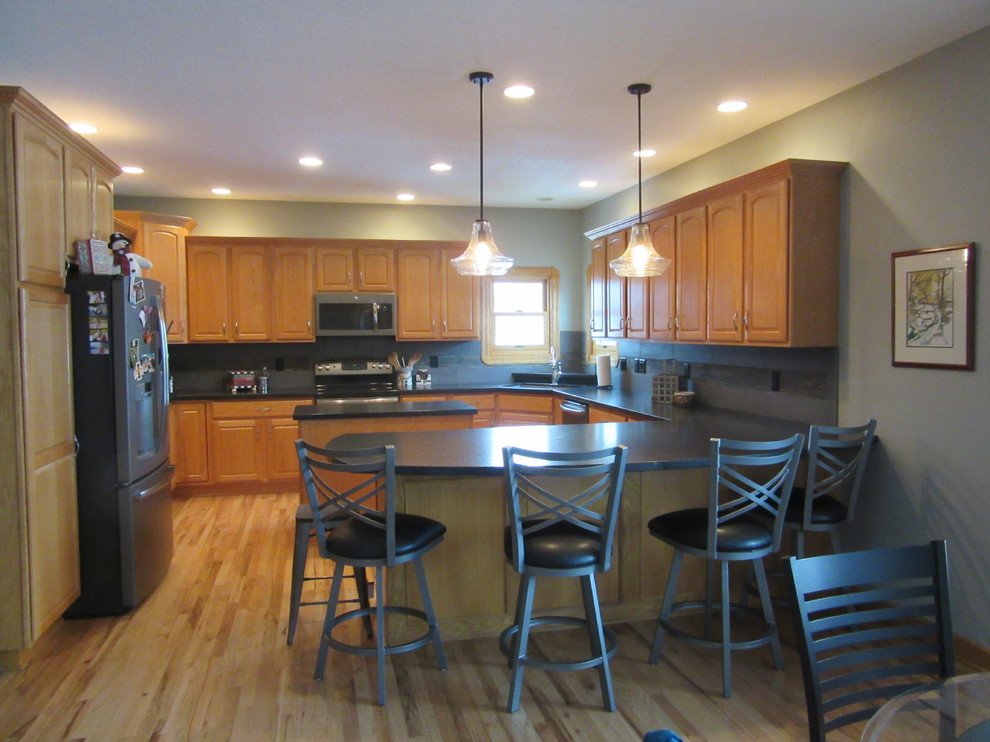 Example of a transitional u-shaped light wood floor eat-in kitchen design with an undermount sink, raised-panel cabinets, medium tone wood cabinets, granite countertops, gray backsplash, ceramic backsplash, black appliances and two islands