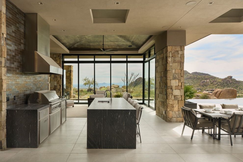 Expansive contemporary back patio in Phoenix with an outdoor kitchen, natural stone paving and a roof extension.