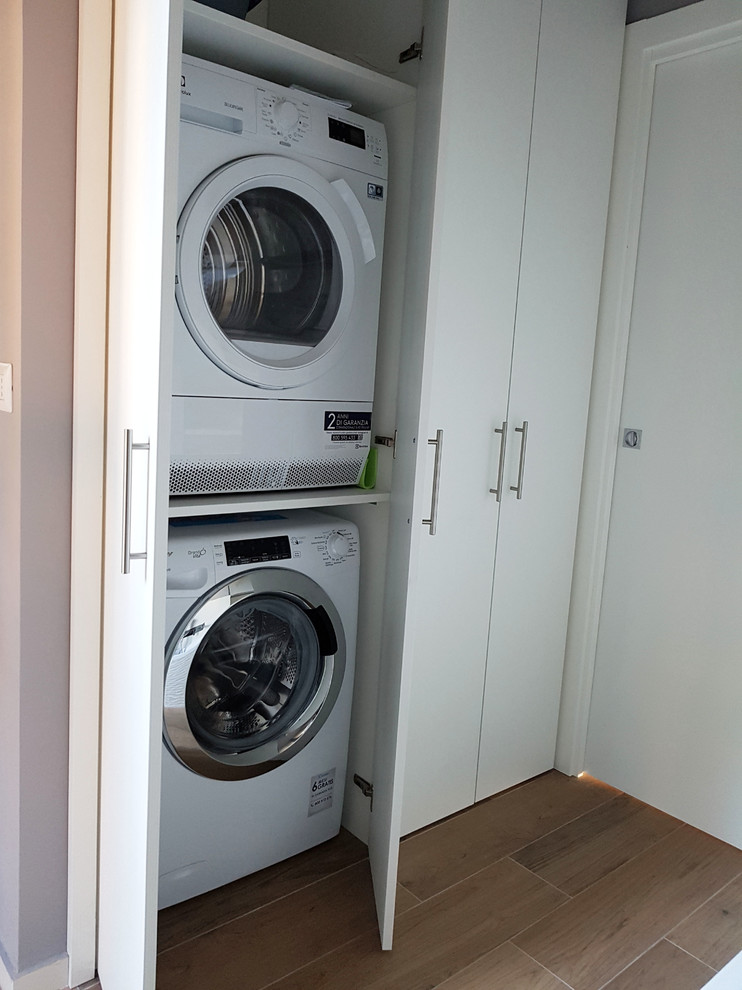 Inspiration for a small contemporary single-wall dedicated laundry room in Milan with flat-panel cabinets, white cabinets, grey walls, porcelain floors, a stacked washer and dryer and brown floor.