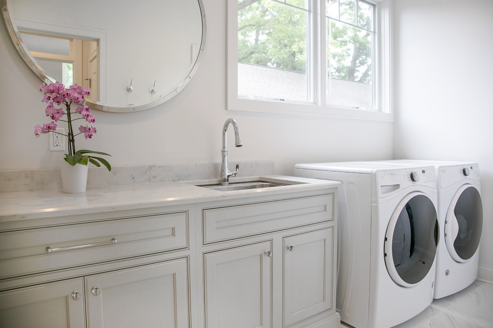 Inspiration for a large transitional single-wall utility room in Milwaukee with recessed-panel cabinets, grey cabinets, quartz benchtops, an undermount sink, white walls, marble floors, a side-by-side washer and dryer and grey floor.