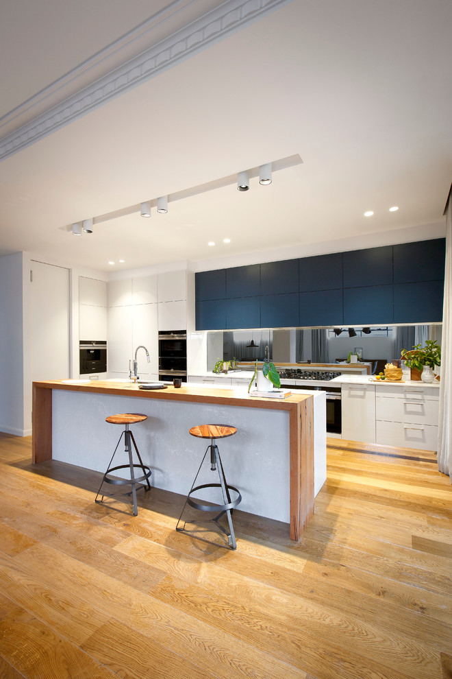Large contemporary kitchen pantry in Melbourne with blue cabinets, quartz benchtops, metallic splashback, mirror splashback, black appliances and with island.
