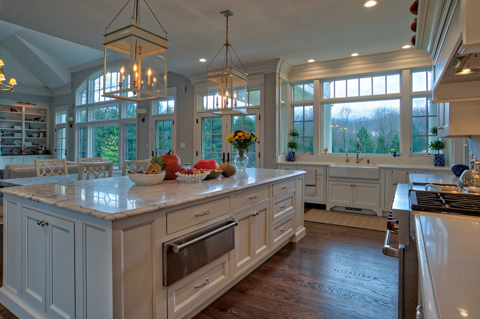 This is an example of a large traditional u-shaped eat-in kitchen in Philadelphia with a farmhouse sink, beaded inset cabinets, white cabinets, quartz benchtops, white splashback, engineered quartz splashback, stainless steel appliances, medium hardwood floors, with island, brown floor and white benchtop.