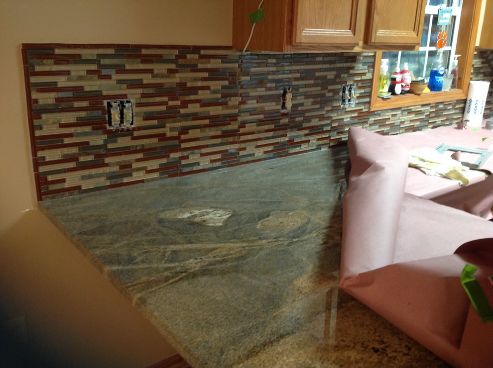 Example of a l-shaped eat-in kitchen design with an undermount sink, flat-panel cabinets, brown backsplash, glass tile backsplash, stainless steel appliances and a peninsula