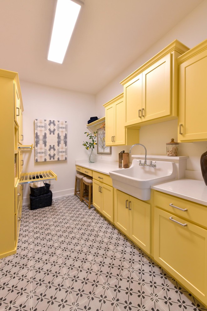 Photo of a traditional dedicated laundry room in Cleveland with a farmhouse sink, shaker cabinets, yellow cabinets, white walls, multi-coloured floor and white benchtop.