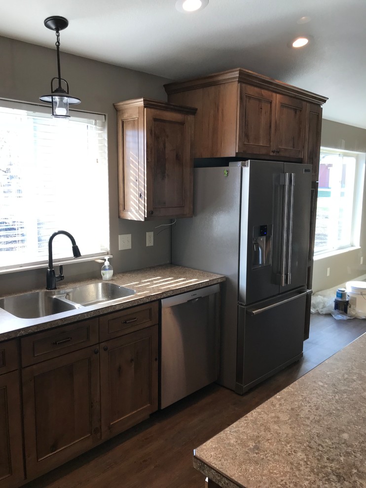 Large mountain style l-shaped medium tone wood floor and brown floor kitchen photo with an undermount sink, recessed-panel cabinets, medium tone wood cabinets, stainless steel appliances, an island and laminate countertops