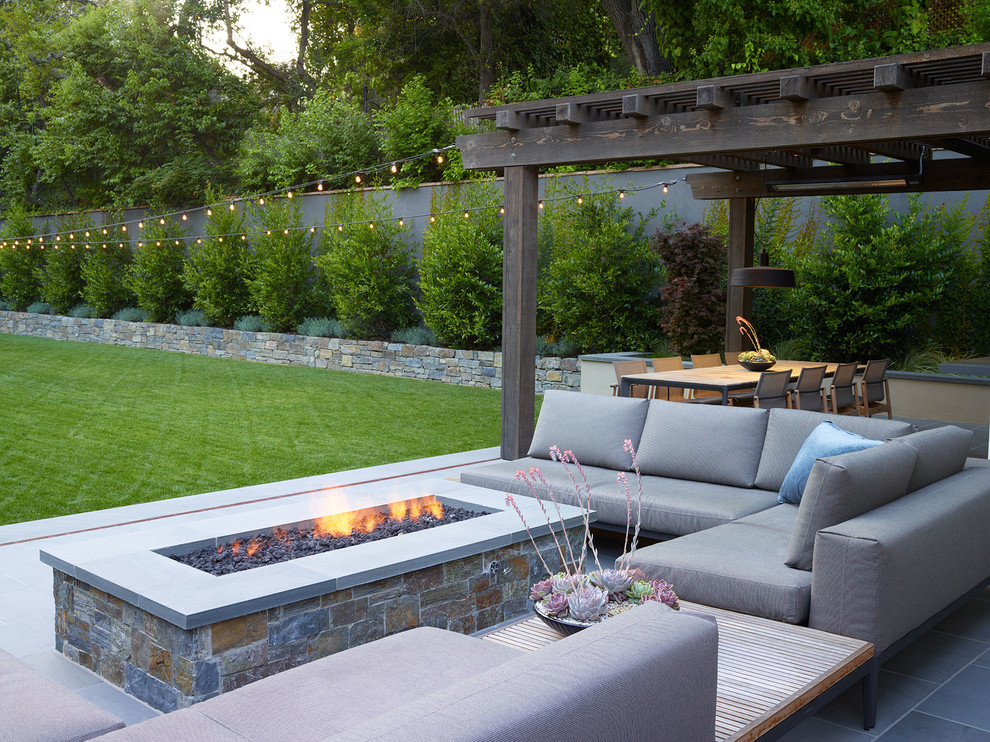 This is an example of a large modern front yard patio in San Francisco with a fire feature and natural stone pavers.