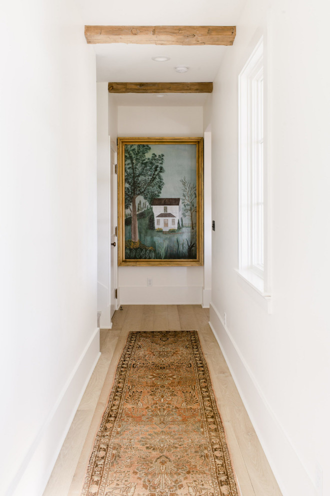 Inspiration for a large country hallway in Dallas with white walls, light hardwood floors, brown floor and exposed beam.