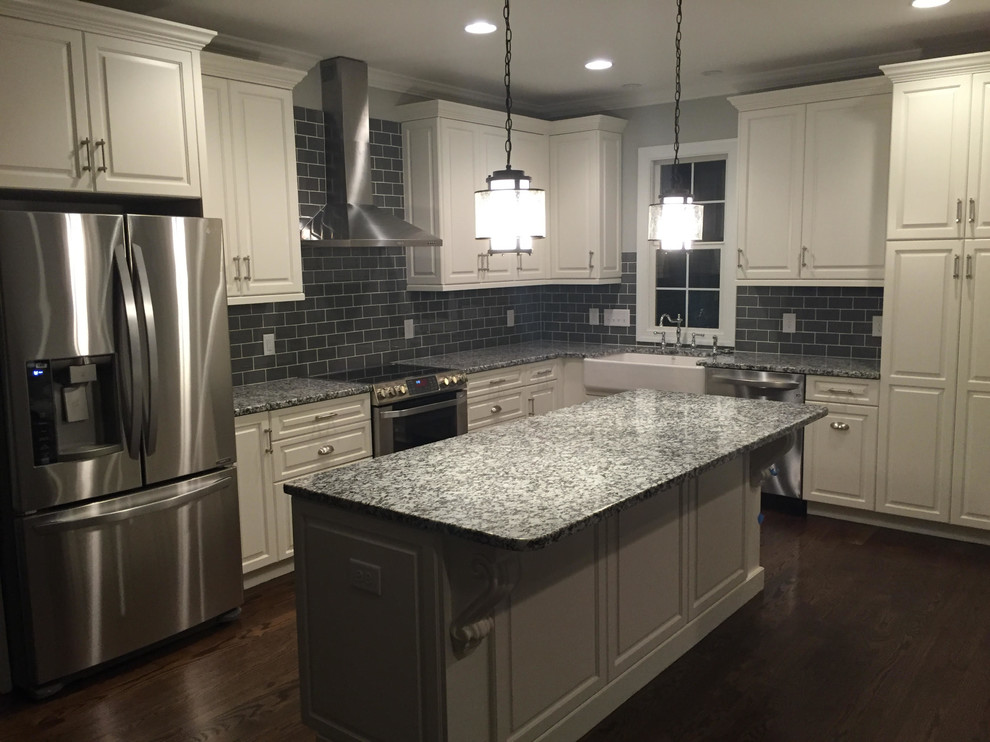 Mid-sized country l-shaped open plan kitchen in Charlotte with a farmhouse sink, raised-panel cabinets, white cabinets, granite benchtops, grey splashback, glass tile splashback, stainless steel appliances, dark hardwood floors and with island.