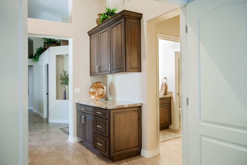 Open concept kitchen - transitional galley porcelain tile open concept kitchen idea in Phoenix with an undermount sink, raised-panel cabinets, dark wood cabinets, granite countertops, beige backsplash, stone tile backsplash, stainless steel appliances and an island